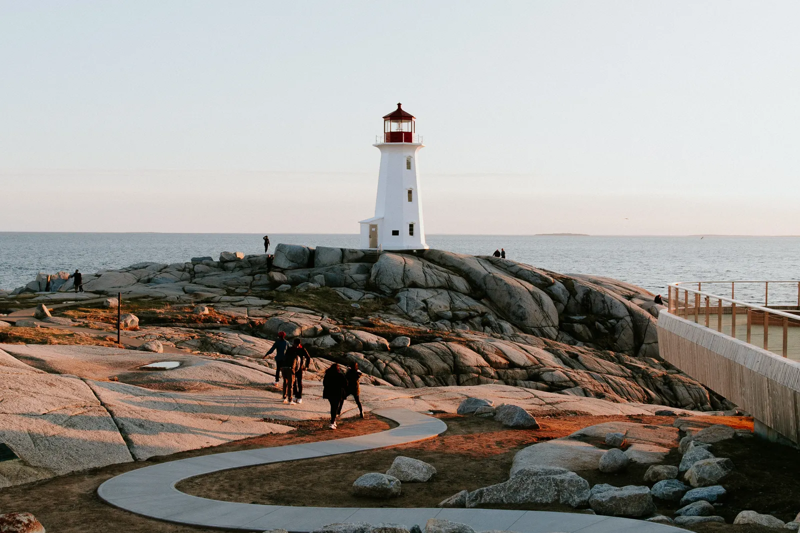 Walkers crossing granite rock toward a lighthouse on the Atlantic coast