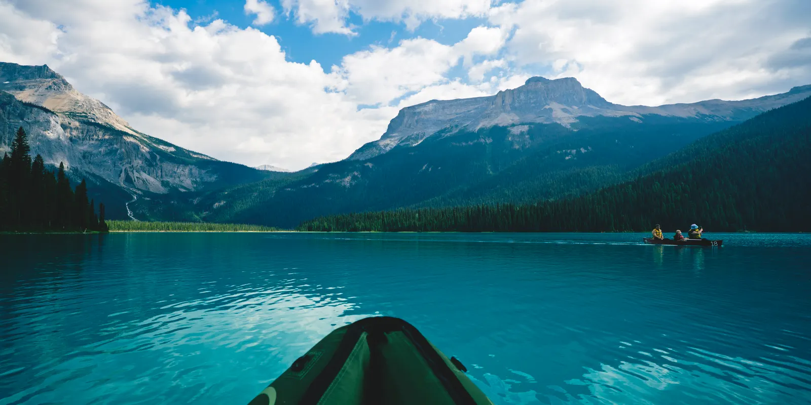A kayaker on the still green water of Emerald Lake beneath forested mountains