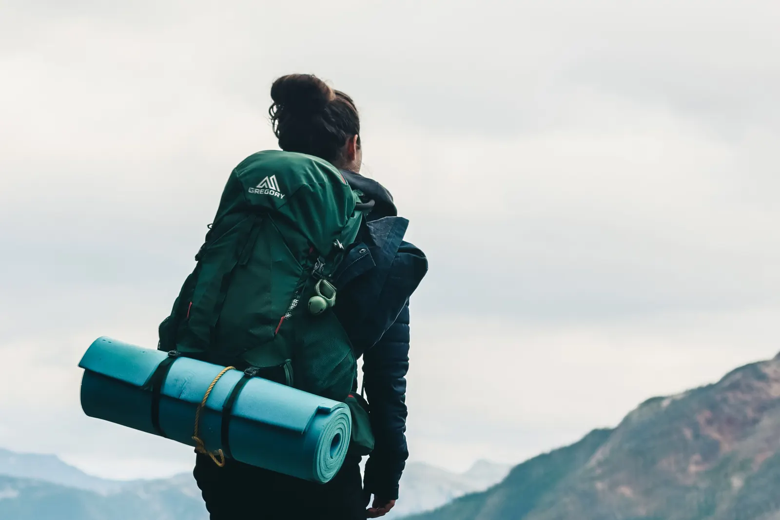 A hiker with a large backpack looking out over a forested valley from a rocky ledge