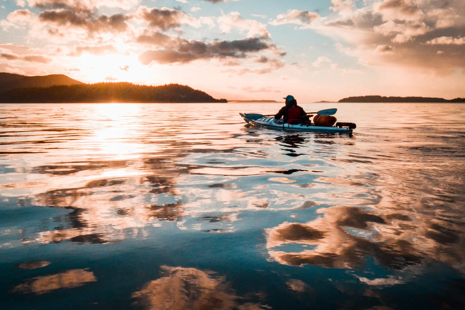 A person paddling a teal kayak on calm water at sunset