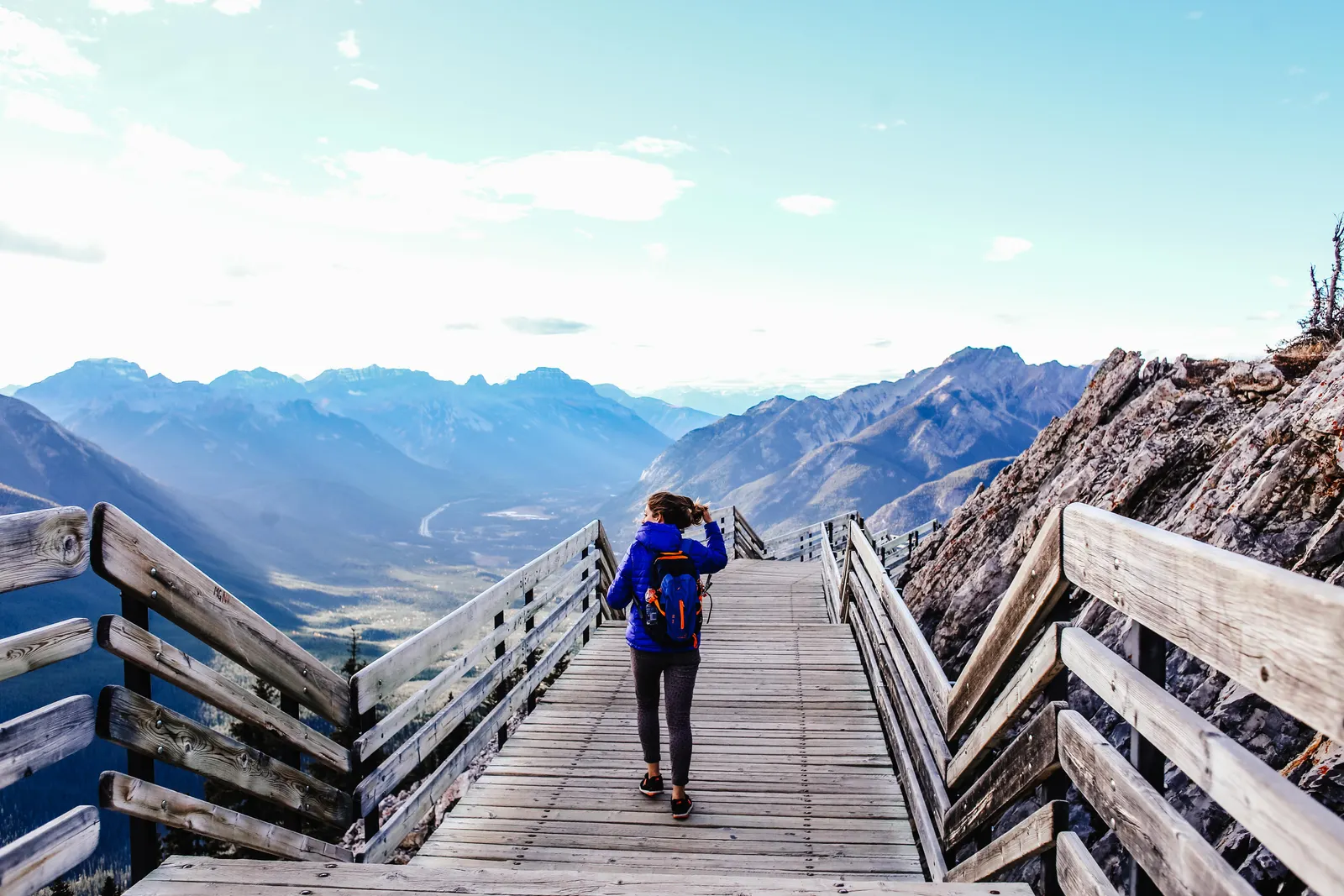A person walking along a wooden boardwalk with mountains in the distance