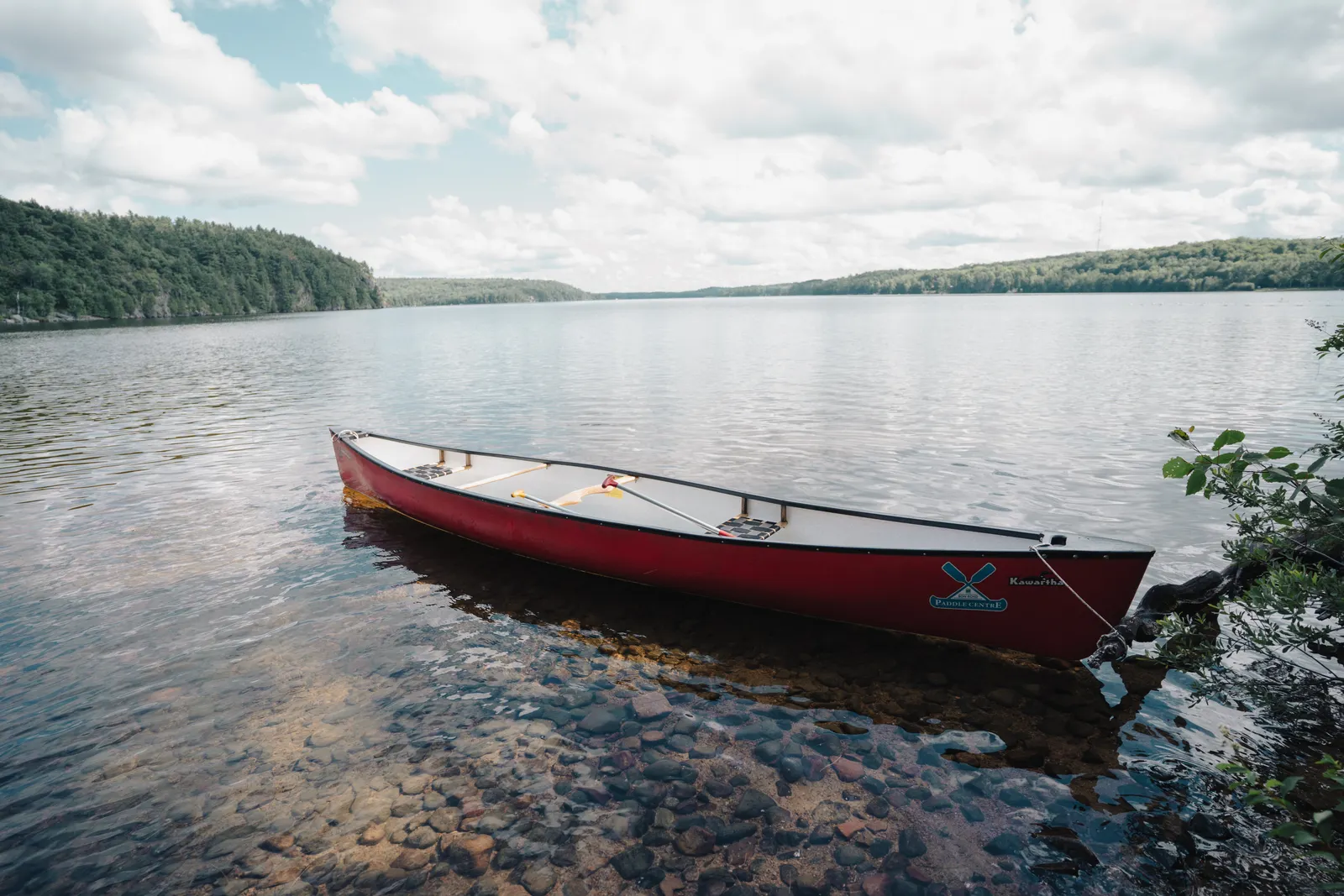 A red canoe on the shore of a quiet forested lake in Ontario