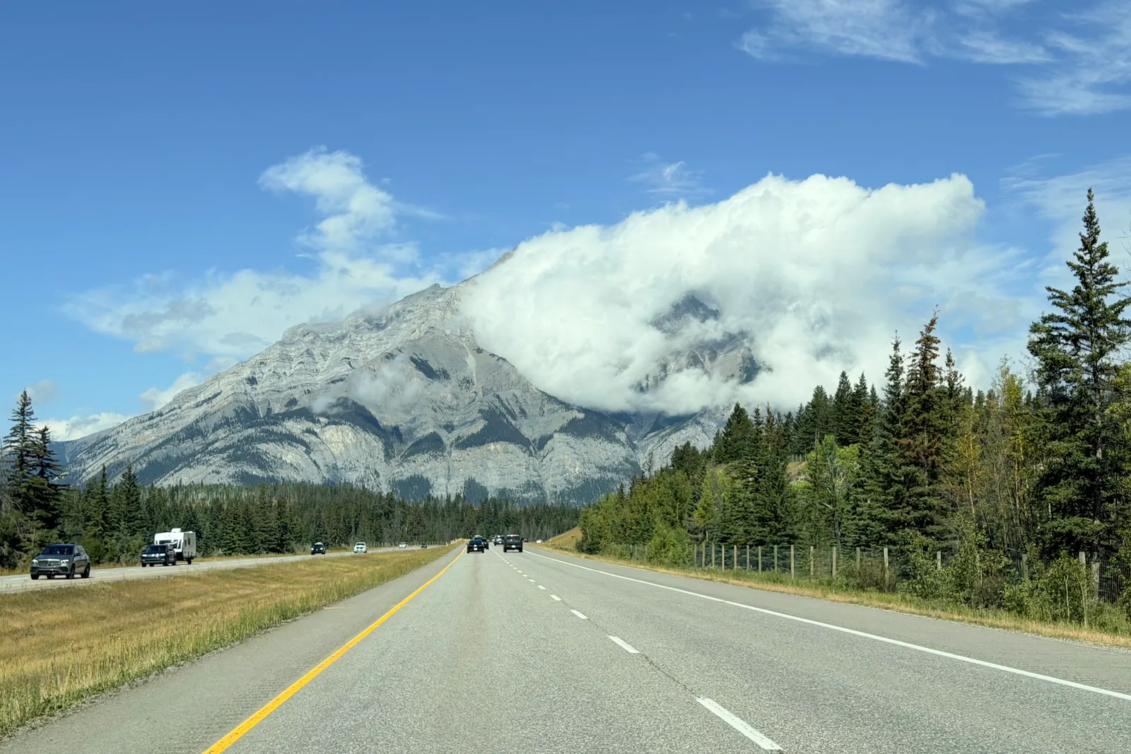 An empty two-lane highway running toward snow-capped Rocky Mountain peaks
